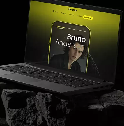 Laptop on textured rock surface displaying Bruno Anderson portfolio website with yellow-green background and iPhone mockup showing contact section